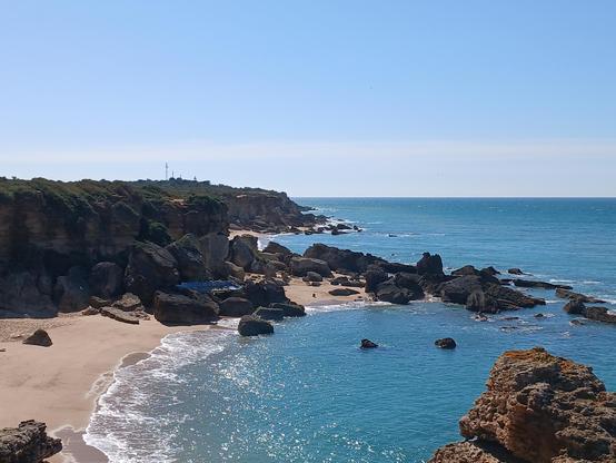 Une crique découpée avec une plage, la mer scintille, bleue comme le ciel