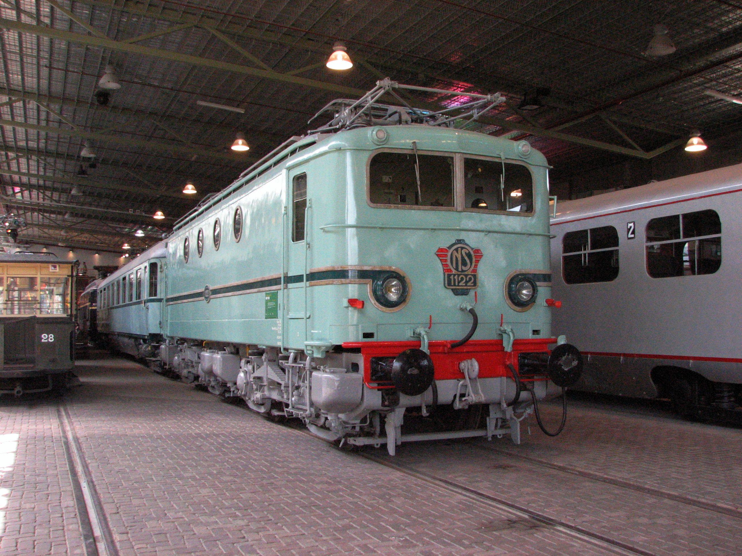 Locomotive série 1100 en livrée vert clair avec bande rouges et vert foncé autour des phares.

Electric locomotive class 1100 in light green livery with red stripe on the front and dark green around the front lights.