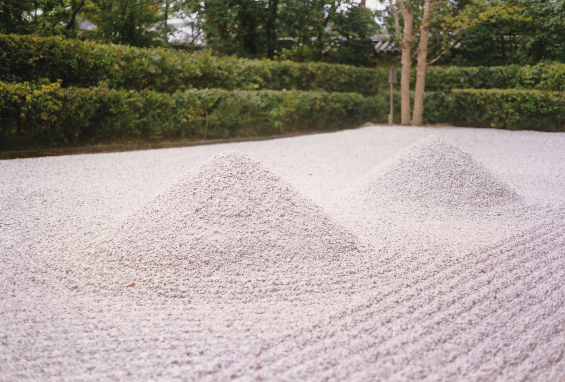Jardin japonais tout de graviers, avec quelques stries et deux monticules en forme de deux monts Fuji, entouré d’une haie verte.