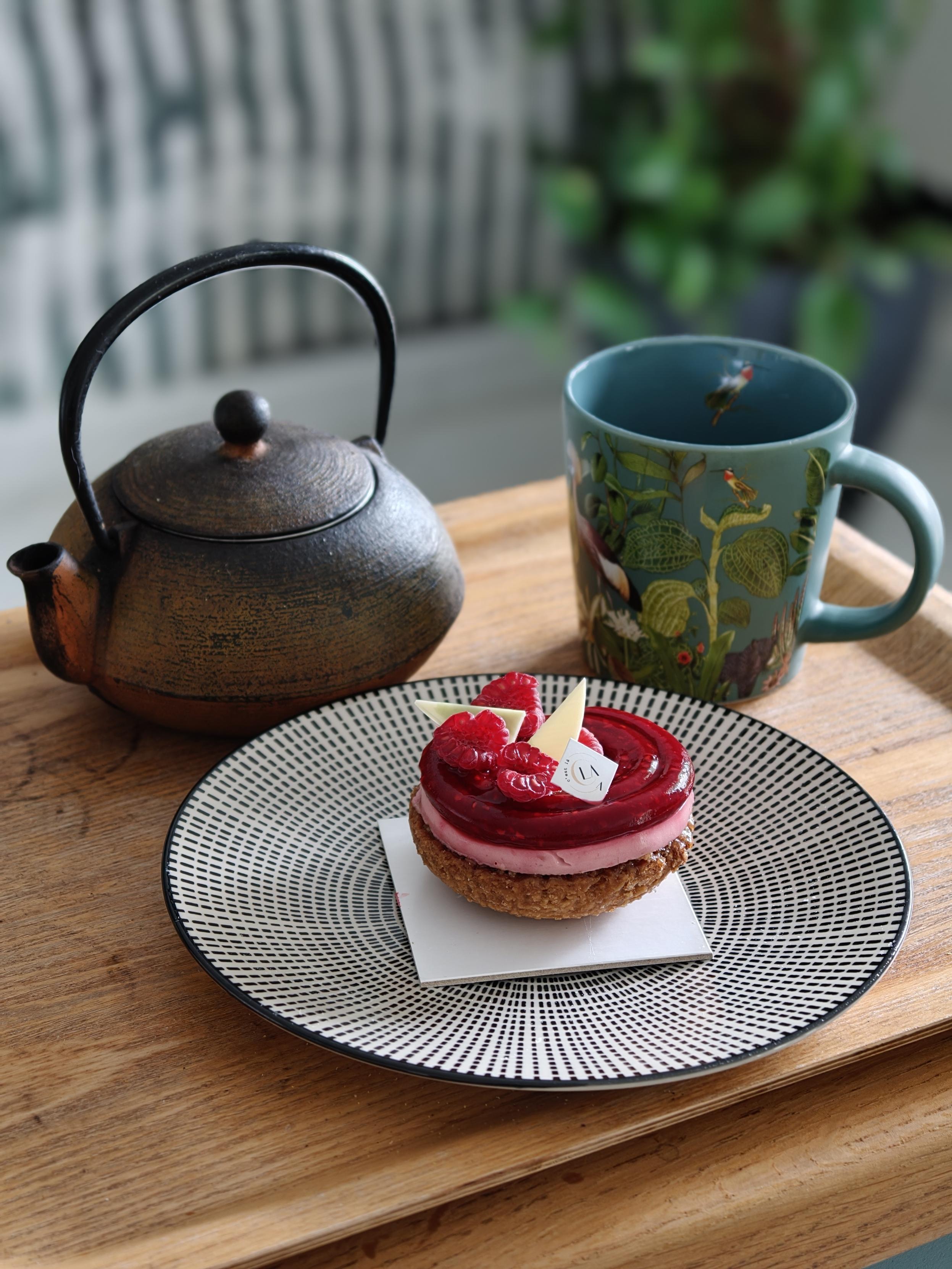 Théière avec une infusion de fleurs de chrysanthèmes, une tasse , une assiette avec un gâteau de pâtisserie avec des framboises, le tout sur un plateau .