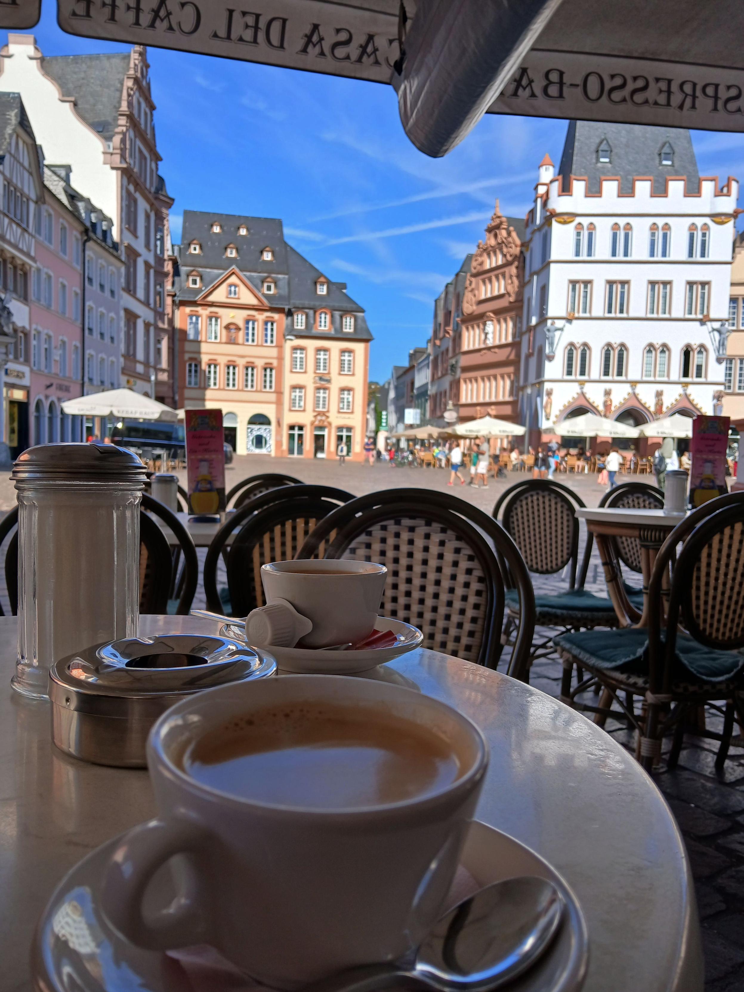 Deux tasses de café italien posées sur une petite table ronde d'une terrasse avec comme arrière-plan quelques bâtiments historiques du centre de Trèves en Allemagne. 

Two cups of Italian coffee placed on a small round table on a terrace with some historic buildings in the center of Trier in Germany as a background.