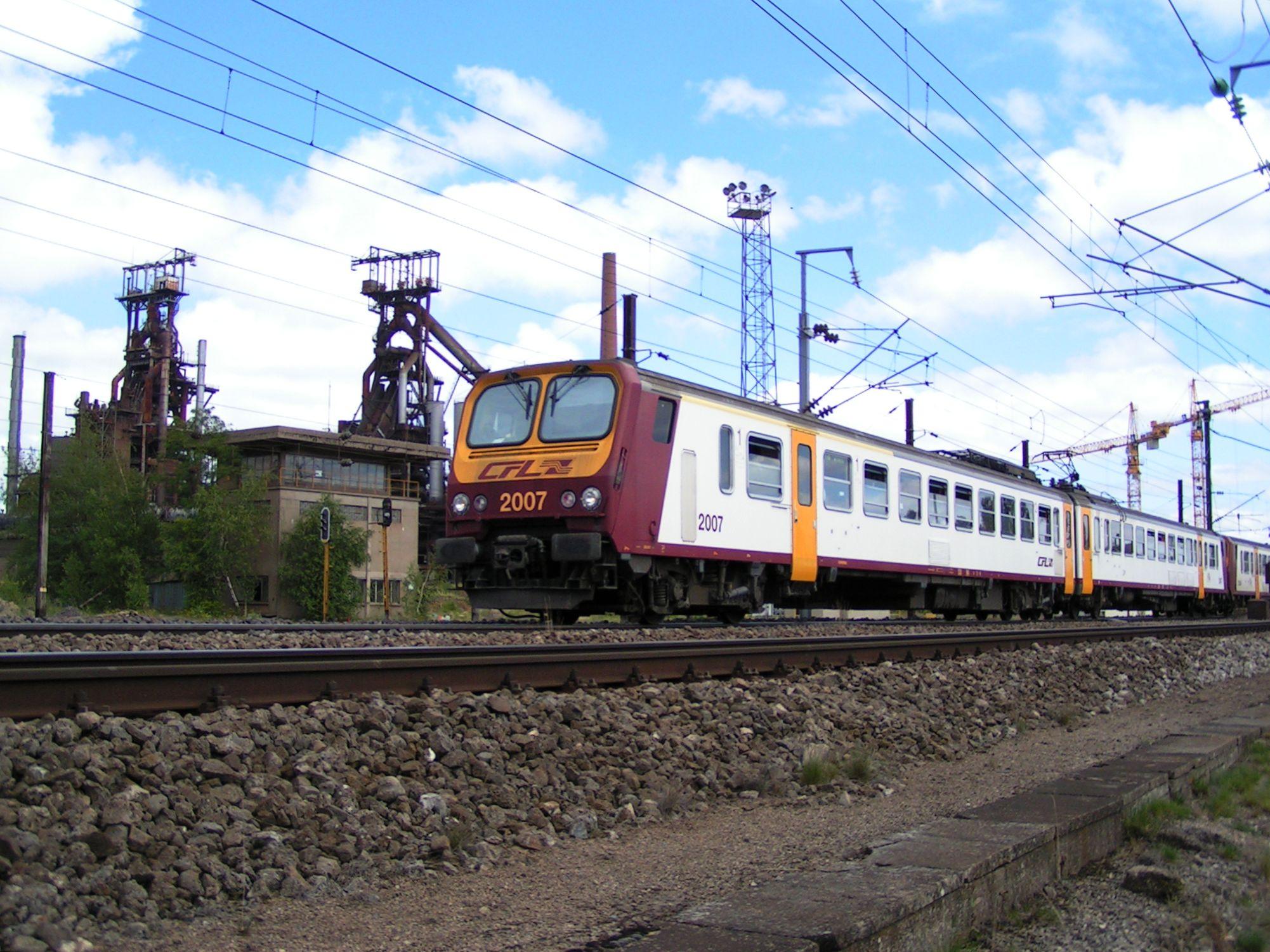 Deux automotrices Z 2000 quittent Belval-Usines vers Rodange avec en coulisse les hauts-fourneaux toujours en service en 2004.

Two EMU Class Z 2000 leaving Belval-Usines towards Rodange with in the background the high furnaces still in use in 2004.
