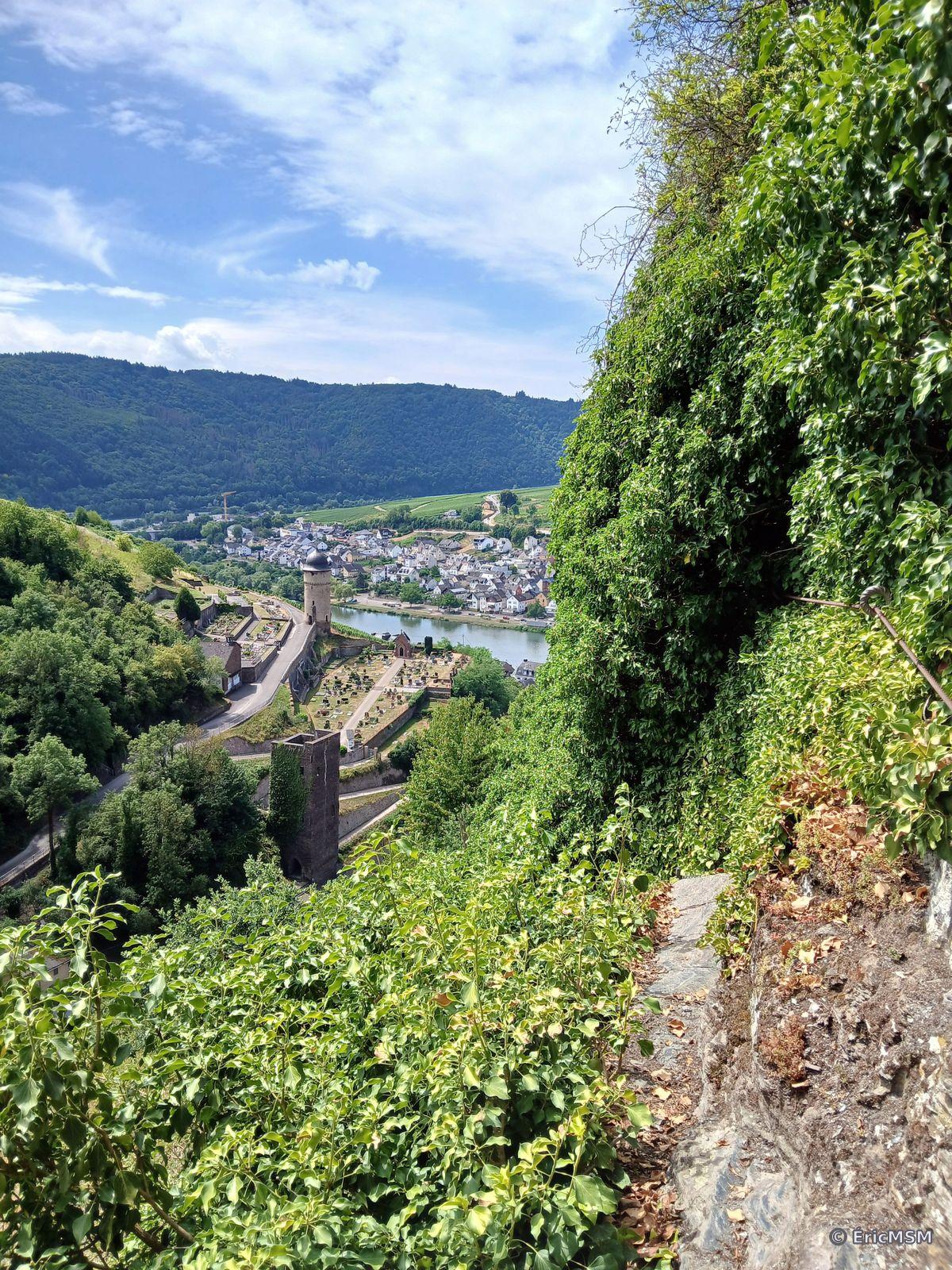Depuis un sentier d'escalade, vue sur la vallée de la Moselle et la petite ville de Zell, deux tours sont visibles, une carrée, et une coiffée en forme de cloche.

From a climbing trail, overlooking the Moselle valley and the small town of Zell, two towers are visible, a square, and a bell-shaped capped.