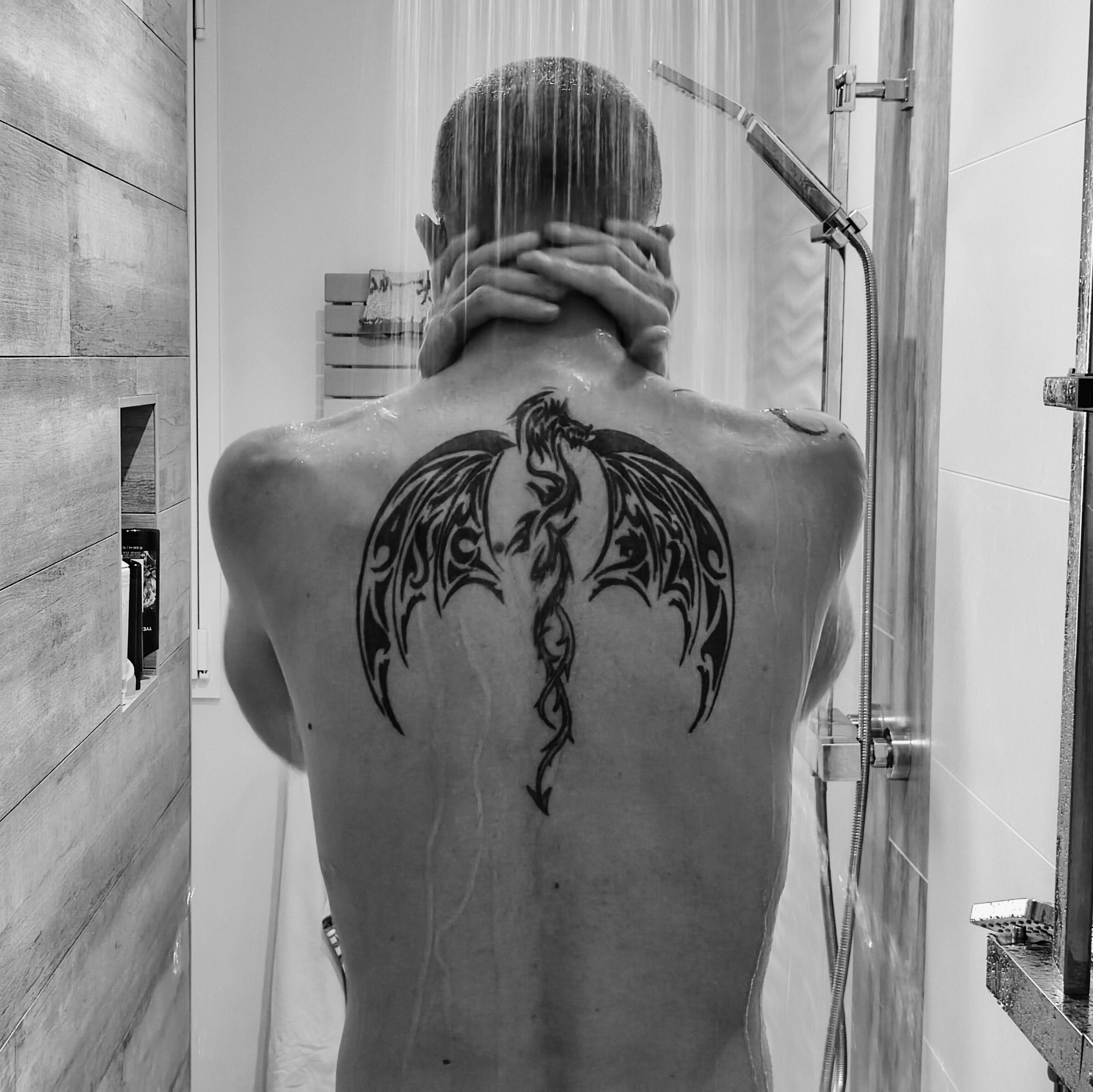 Homme de dos sous la douche avec un tatoiage dans le dos