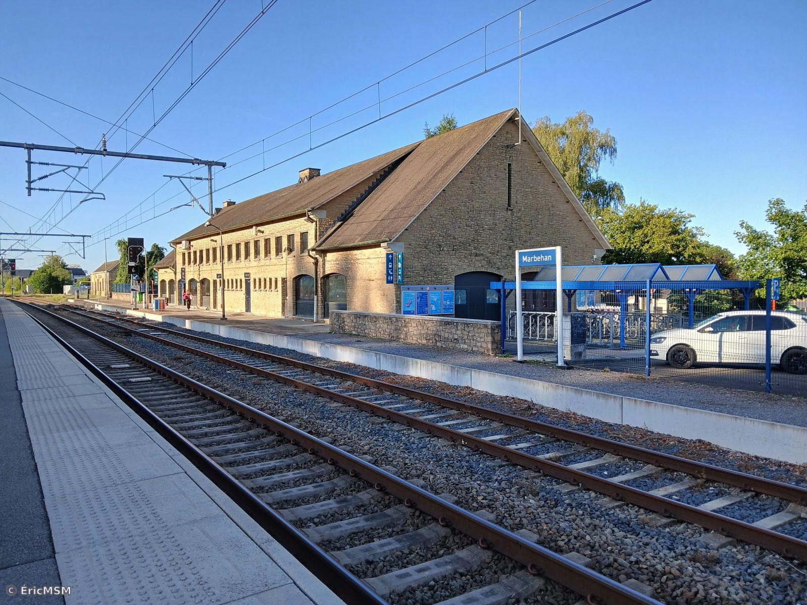 Un bâtiment de gare vue depuis le quai central, il y a une voie le long de la gare et une seconde en premier plan le long du quai.

A station building seen from the central platform, there is a track along the station and a second in the foreground along the platform.