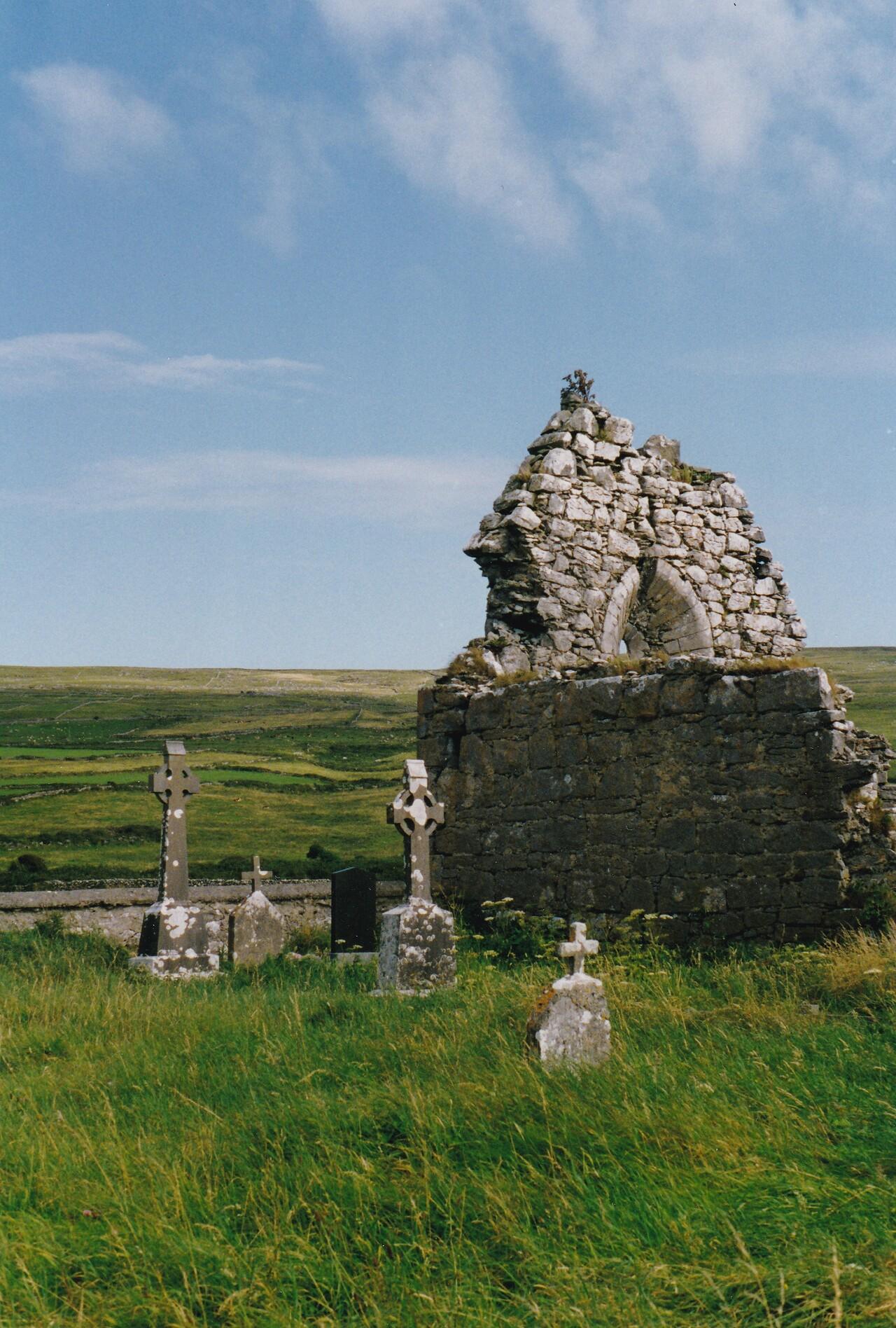 Ruines d’une ancienne église en pierres avec de vieilles croix également en pierres formant cimetière, sur l'herbe verte de la lande irlandaise dans la région du Kerry.