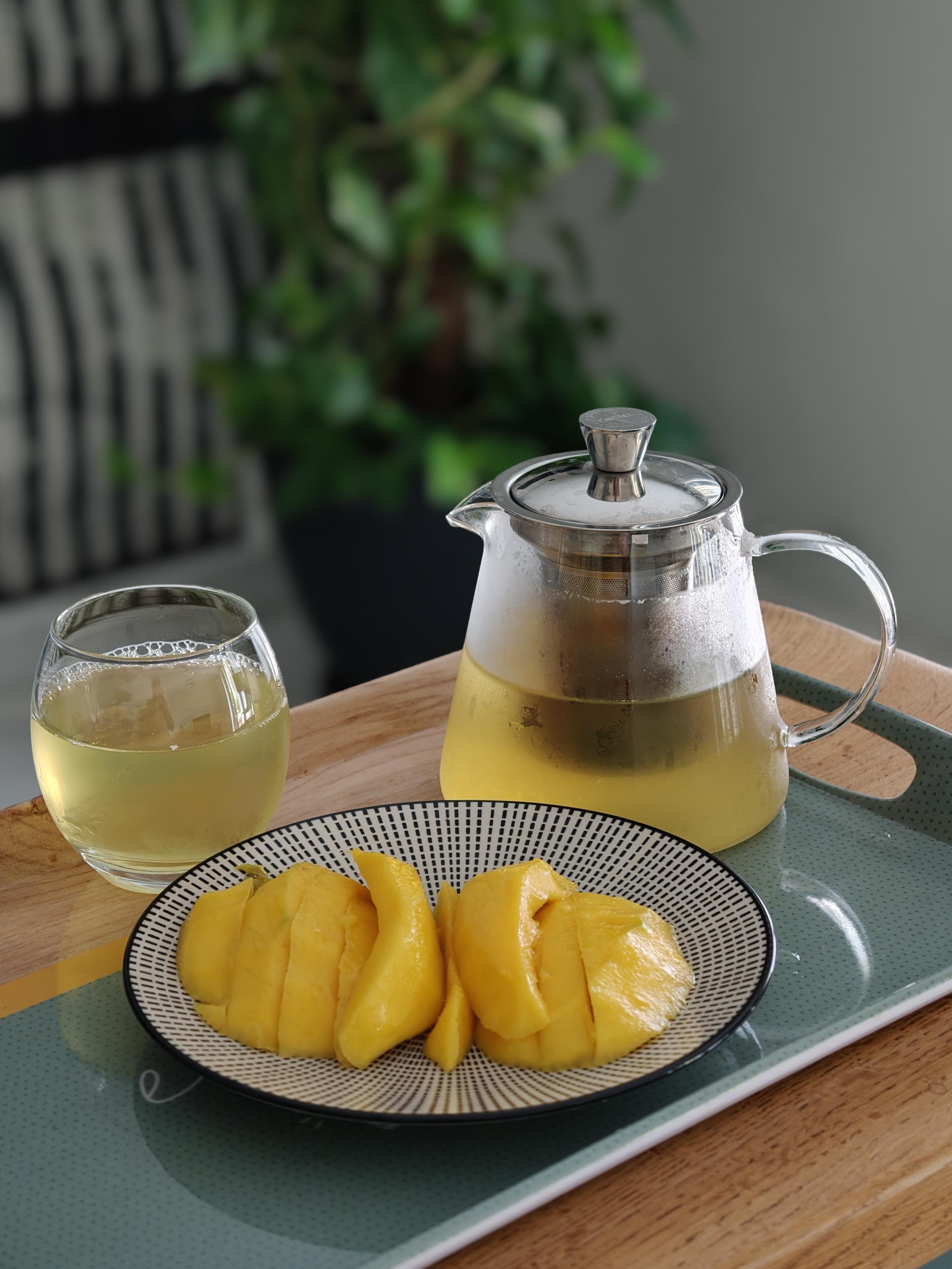 Théière et verre avec infusion de thé glacé. Dans l'assiette une mangue découpée