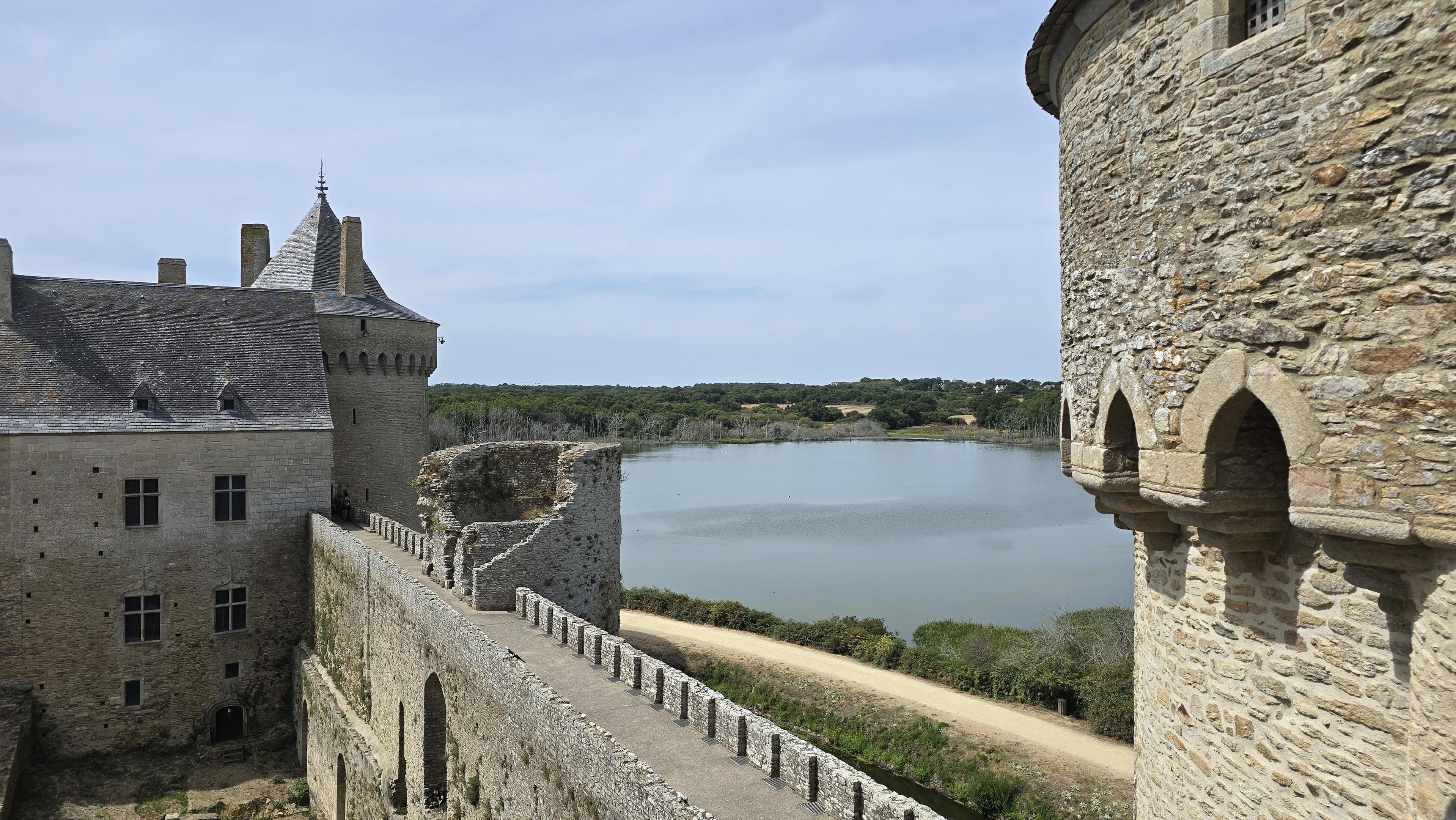 Vue d’un étang depuis le château de Suscinio dans le Morbihan. Sur la droite une tour ronde, au premier plan un chemin de ronde à créneaux, sur la gauche un corps de bâtiment.