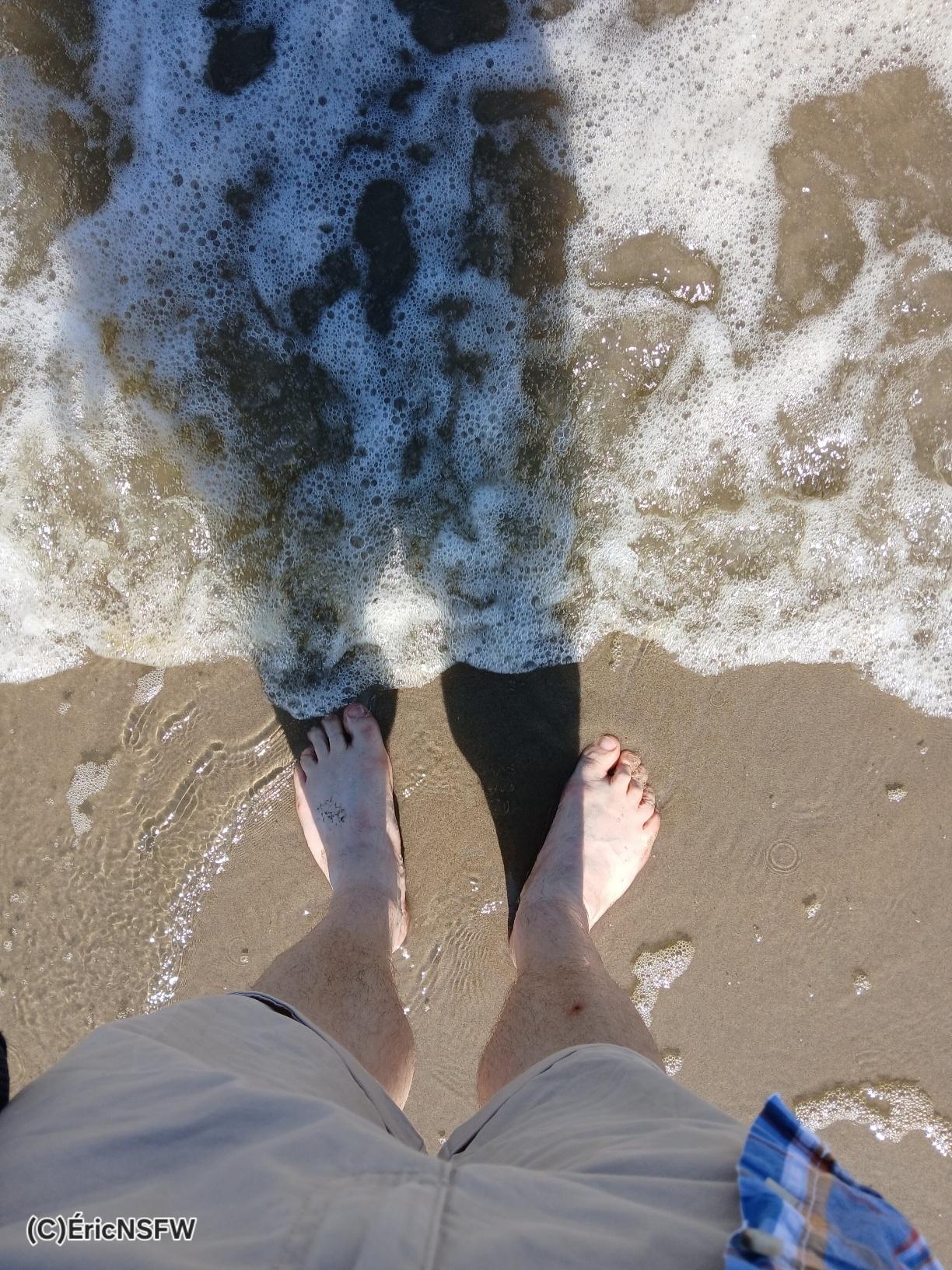 Les jambes poilues d’un homme mature au bord de la mer, les pieds dans le sable.